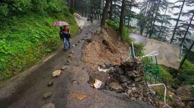 Commuters walk on a road, partially washed away due to heavy rainfall, in Shimla.